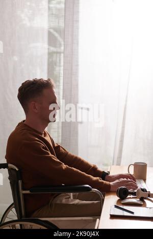 Serious young man in wheelchair working on computer at home Stock Photo