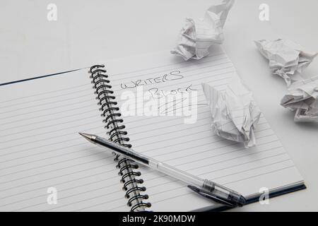 Open book with a pen and a note saying writers block with crumpled paper to one side. Stock Photo