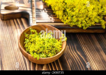 Galium verum, lady bedstraw or yellow bedstraw used in alternative medicine in wooden plate on a vintage table next utting boards. Medicinal herbs Stock Photo
