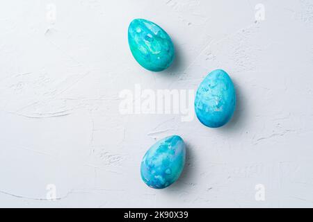 Three colorful hand-painted Easter eggs scattered on a white textured background, minimalist flat lay. Stock Photo