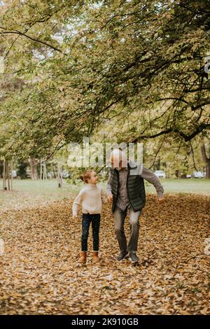 Handsome grandfather spending time with his granddaughter in park on autumn day Stock Photo