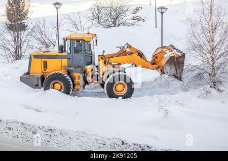 Snow clearing. Tractor clears the way after heavy snowfall. A large orange tractor removes snow from the road and clears the sidewalk. Cleaning roads Stock Photo