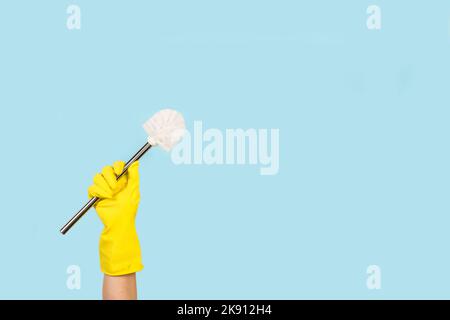 Woman hand with yellow rubber glove holding a toilet brush on a light blue background with copy space Stock Photo