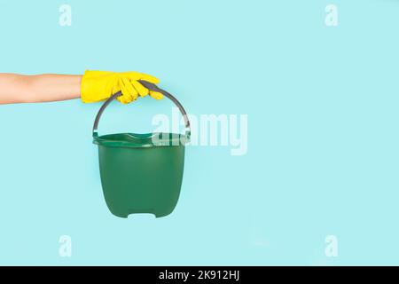 Woman hand with yellow rubber glove holding a green pail on a light blue background with copy space Stock Photo