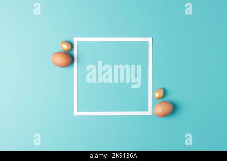 Easter beige and golden eggs on blue background with white frame. Flat lay, copy space. Stock Photo