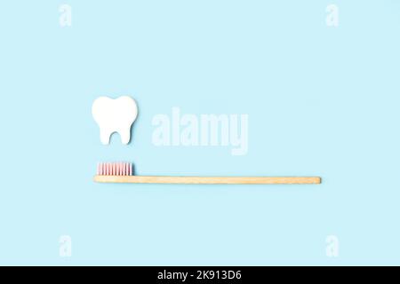 Bamboo wood toothbrush with pink brush bristles and a white wooden molar on a light blue background with copy space Stock Photo