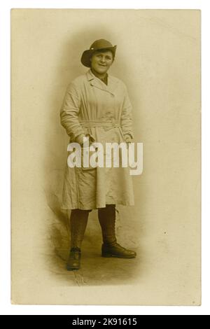 Original WW1 era studio portrait postcard of typical young Welsh Land Girl,  looking happy, wearing the standard uniform of breeches, felt hat, a knee-length overall tunic (with a button-fastening integrated belt) leather leggings and boots, U.K. dated 1918, photograph by Chapman of Swansea, Wales, U.K.