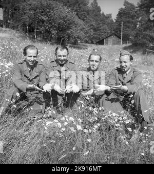 Military men in the 1940s. Four men in uniform are sitting in a meadow flowered field, holding their hands in front of them, palms up. A gesture that means something but not known what.  Sweden 1940. Kristoffersson ref 149-6 Stock Photo