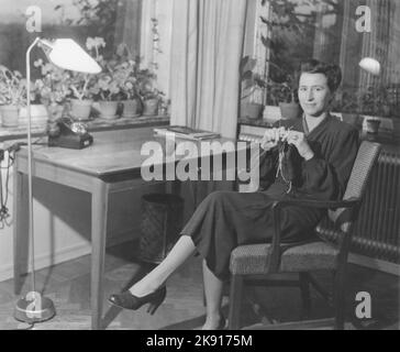 Woman in the 1940s. A young dark-haired woman at home knitting something when sitting in the chair at her desk. Sweden 1948 Stock Photo