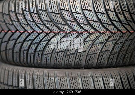 Full frame abstract background of texture of black winter tires with simple tread pattern stacked together in row Stock Photo
