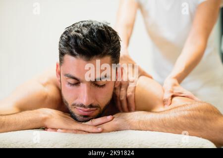 Handsome bearded male client of massage salon lying on table and getting back massage on resort spa Stock Photo