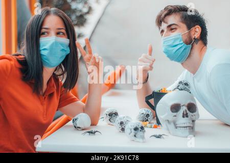 Two friends boy and girl taking a selfie in medical masks while making Halloween skull gang decorations Stock Photo