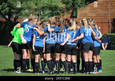 A soccer team of girls wearing blue uniform chants in a huddle Stock Photo