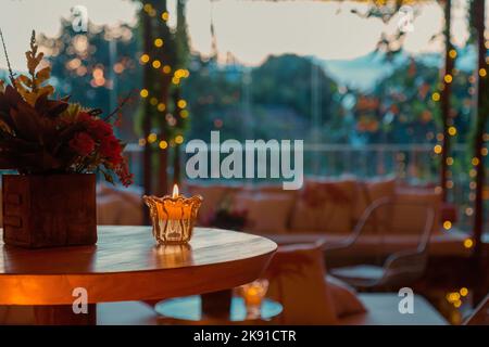 A warm interior design of a terrace with a wooden table and a candle on it on a bokeh background Stock Photo