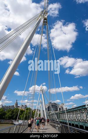 Golden Jubilee Bridge next to Hungerford railway bridge over the River Thames, London, UK. People walking across the pedestrian bridge with cables Stock Photo
