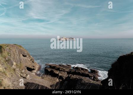 A view from the coast to the Faro de la Isla de Mouro under the blue sky Stock Photo