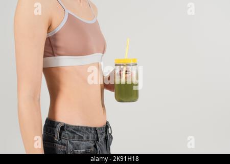 cropped view of fit woman in sports top holding fresh smoothie isolated on grey Stock Photo