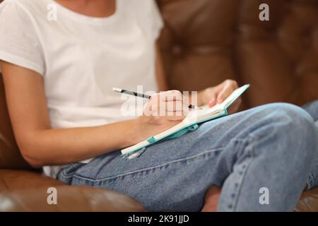 Woman sitting on sofa and writing something on notepad Stock Photo
