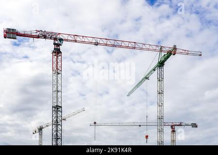 Several tall construction tower cranes in city construction sites against cloudy sky background Stock Photo