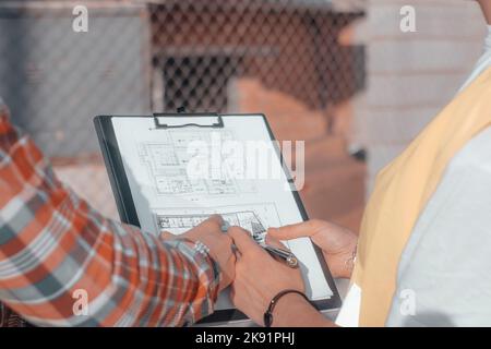 A closeup of a pair of builders pointing at the construction design while standing near the construction site Stock Photo