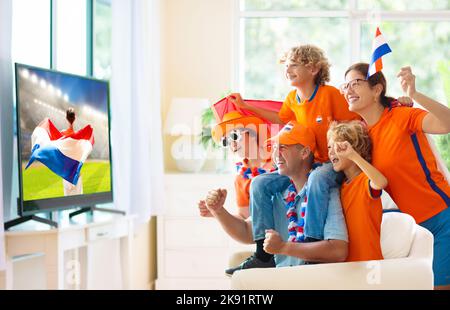 Group of Netherlands football fans watch tv at home. Go Holland. Friends watching Dutch soccer match in white living room. Stock Photo