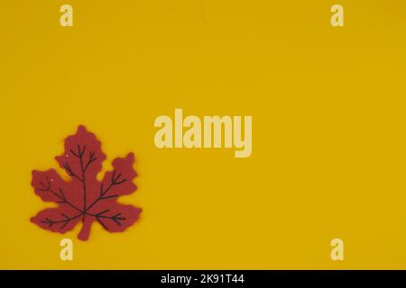 Red felt leaf in bottom left corner with yellow background and copy space Stock Photo
