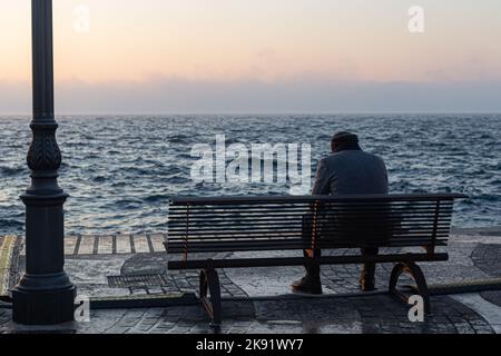 An old man sitting alone on the bench in front of the lake Stock Photo