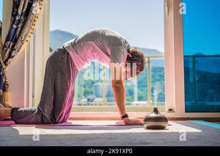 Mindful healthy man practicing yoga at home. Sitting on the floor doing yoga for mental balance relaxing on stress. Enjoying time uses an aroma Stock Photo