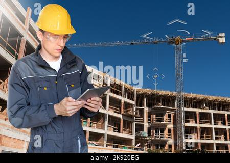 Builder with a digital tablet controls a remote-controlled unmanned crane. Digital transformation in construction industry.  Stock Photo
