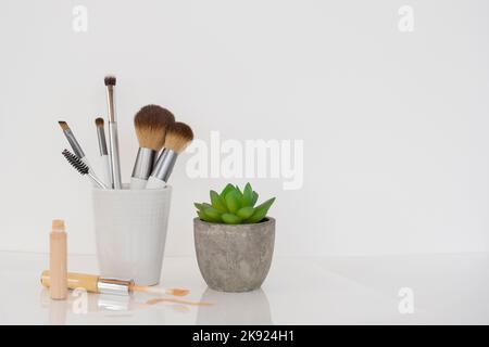 Countertop with white jar of makeup brushes, concealer, and a cactus plant. Stock Photo