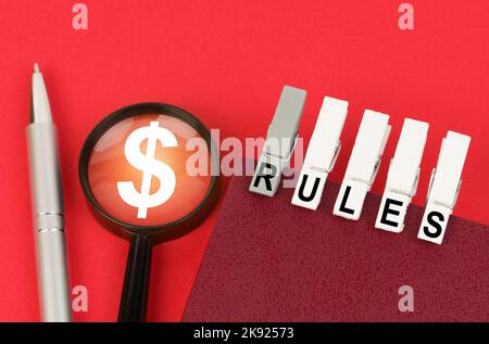 Business concept. On the red surface is a pen, a magnifying glass with a dollar symbol and a notepad with clothespins and the inscription - RULES Stock Photo