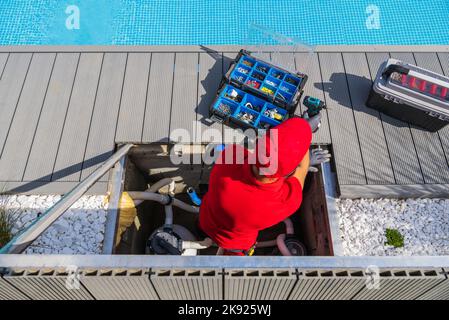 Professional Technician in Red Uniform Performing Regular Pool Maintenance Procedures. Open Toolbox with Different Tools and Components in Front of Hi Stock Photo