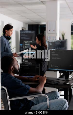 It programmer in wheelchair typing html code in coding office, working on server program with computer. African american web developer with chronic disability writing script with system algorithms. Stock Photo