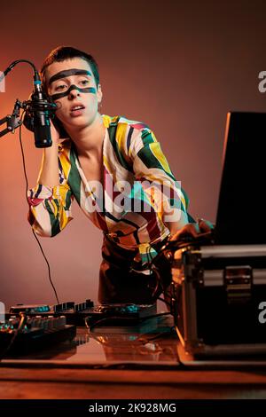 Woman performer producing techno music at mixer, having crazy make up and playing with audio stereo equipment. Artist mixing sounds at turntables to make musical performance in studio. Stock Photo