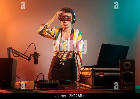 Female musician suffering from headache and pain, feeling stressed and unwell before mixing techno song on dj turntables. Artist performer feeling miserable and hurt from migraine. Stock Photo