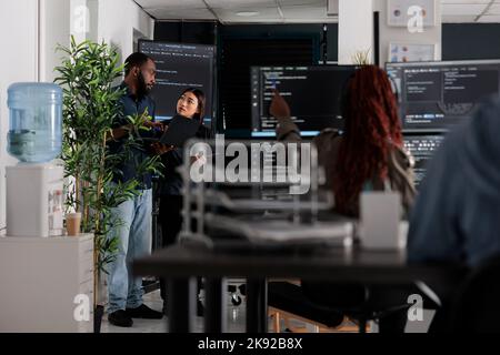 Engineers checking artificial intelligence code looking for errors on laptop, checking big tv monitor in it agency office. Programmers working on cyber security innovation in busy software company Stock Photo
