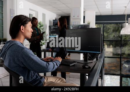 App engineer looking at computer typing machine learning server code, sitting at desk in software company. Cloud developer working on database system with coding script in it busy office Stock Photo