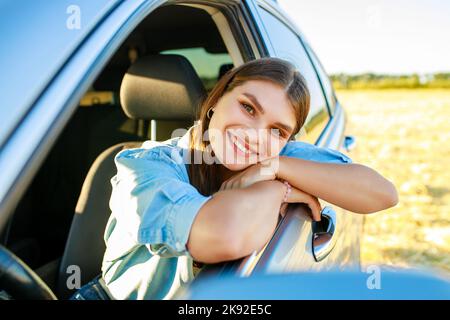 Attractive young woman in blue shirt at sunset light with her car Stock Photo
