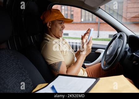 Side view portrait of female delivery driver using smartphone app in van Stock Photo