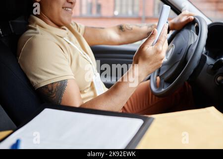 Close up of tattooed woman driving delivery van and using mobile app Stock Photo