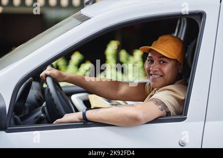 Side view portrait of female delivery worker smiling at camera from van window Stock Photo