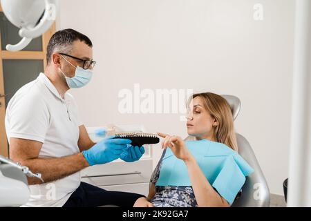 Consultation with dentist about teeth whitening and showing girl patient teeth color shades guide in dental clinic. Dentistry. Woman looking at teeth Stock Photo