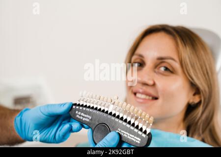 Teeth color shades guide with woman patient. Tooth whitening. Dentist working with teeth color matching samples in dental clinic. Dentistry Stock Photo