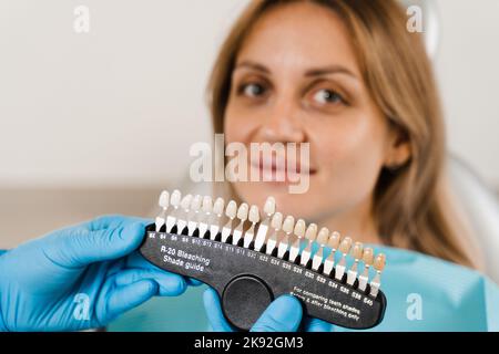 Teeth color shades guide with woman patient. Tooth whitening. Dentist working with teeth color matching samples in dental clinic. Dentistry Stock Photo