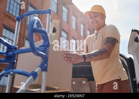 Low angle portrait of female delivery worker unloading cardboard boxes in sunlight, copy space Stock Photo