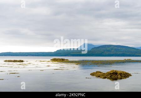 The calm,tranquil summer sea,late afternoonon the Loch,rocks protruding from the water's surface looking towards the distant mountains near Elgol,on t Stock Photo