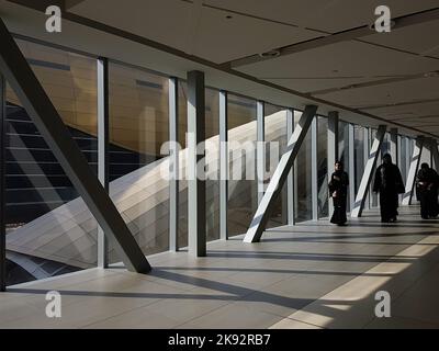 Three Arabic women wearing black Shaylas and Abayas walk through Dubai Mall Metro Link Bridge. Geometric interior. Day in modern Middle East city. Stock Photo