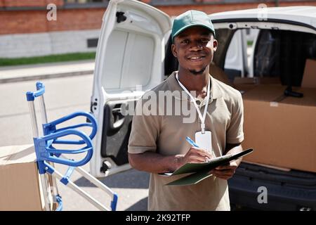 Waist up portrait of black young man unloading van with packages and smiling at camera Stock Photo