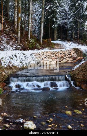 Walking path through the trees with snow next to a creek running over rocks on a cold autumn day in the Bavarian Alps of Gemrany. Stock Photo