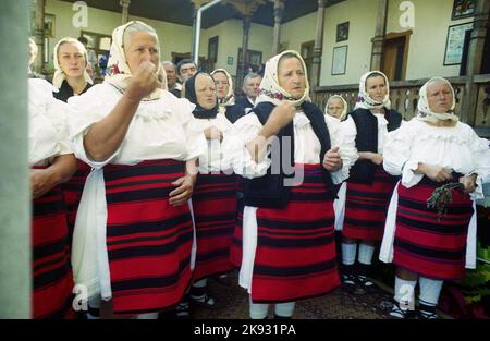 Maramures, Romania. Elderly women of Eastern orthodox faith praying and crossing themselves during a religious ceremony. Traditional handmade folk costumes. Stock Photo